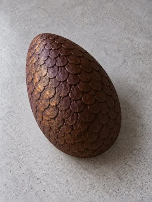 A whole finished chocolate dragon egg, scales dusted aubergine and gold